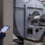 echnician reviewing wireless vibration measurements from a protected position near an industrial fan.